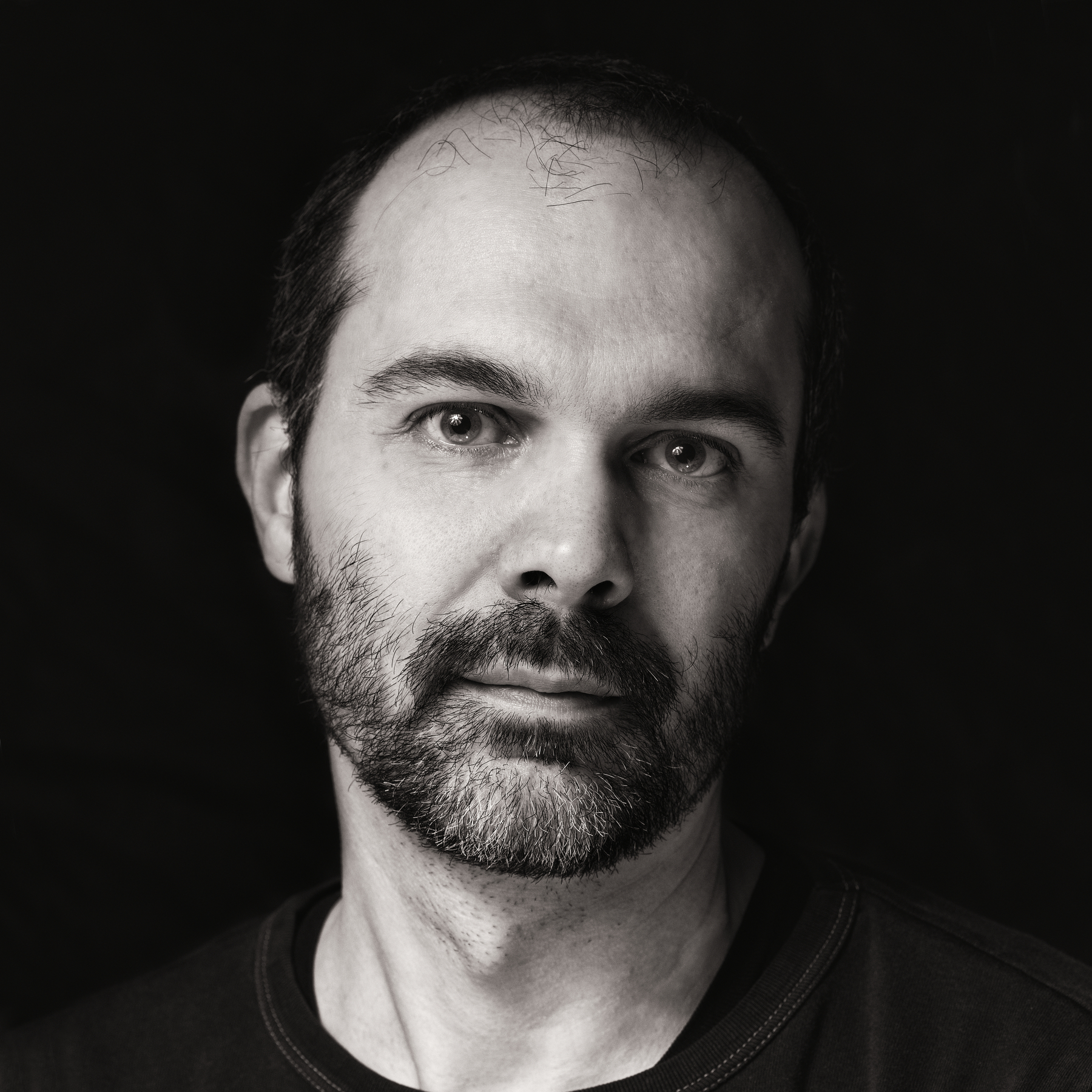 Auto-generated description: A black and white portrait of a man with a beard against a dark background.